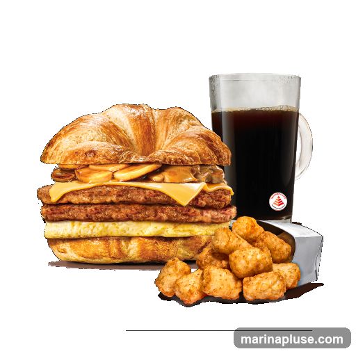 A tall breakfast sandwich on a croissant with multiple sausage patties, cheese, and mushrooms, served with a side of tater tots and a mug of steaming black coffee. A small red and white logo is visible on the coffee mug.