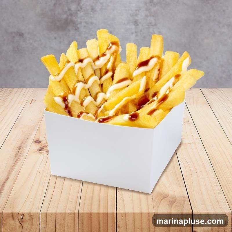 A white box filled with golden french fries, drizzled with a creamy white sauce and a dark brown sauce. The box sits on a wooden table with a grey textured background.