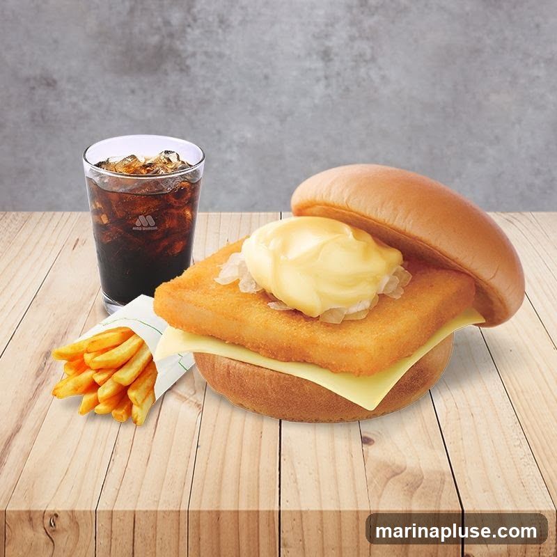 A fish burger with cheese, tartar sauce, and onions, served with a side of french fries and a glass of cola with ice. The meal is presented on a wooden table with a grey textured background.