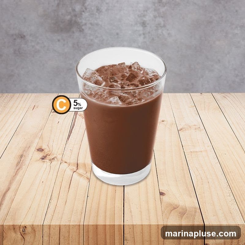 A glass of chocolate drink filled with ice cubes sits on a wooden table. A circular graphic with a 'C' and '5% sugar' is visible on the left side of the glass. The background is a textured gray wall.