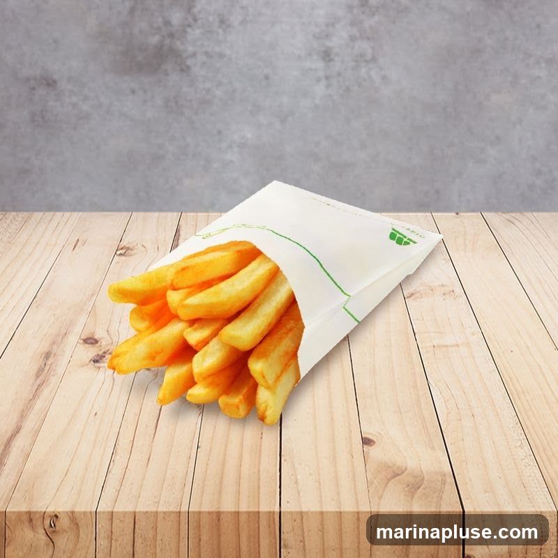 A white paper container filled with golden-brown french fries sits on a wooden table. The container has a green line design and a small green logo on the right side. The background is a textured gray wall.