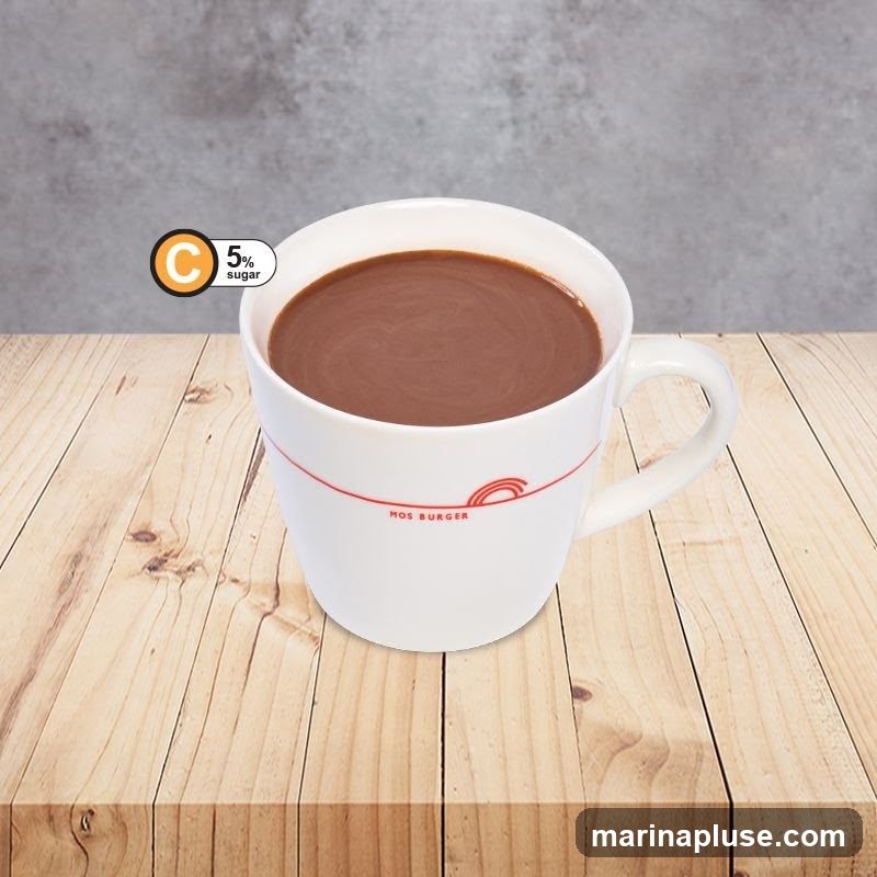 A white mug filled with hot chocolate sits on a wooden table. The mug has a red line around it with the text "MOS BURGER" and a red arch logo. A circular graphic in the upper left corner indicates "C 5% sugar". The background is a textured gray wall.