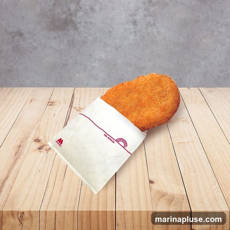 A golden-brown, oval-shaped fried patty is partially wrapped in a white paper sleeve. The sleeve has a red outline and a small red logo on the left side. Text on the sleeve reads "NOS BURGER" and features a stylized rainbow graphic. The patty and wrapper rest on a light-colored wooden surface, with a textured gray background behind it.