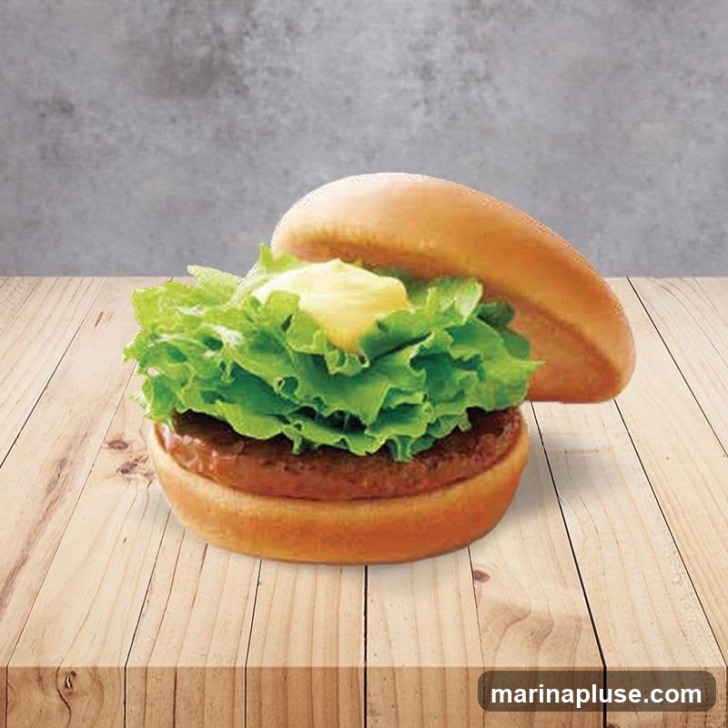 A close-up shot of a burger with a thick patty, a generous amount of fresh green lettuce, and a dollop of yellow sauce, all nestled between a soft bun. The burger is placed on a wooden surface with a textured grey background.