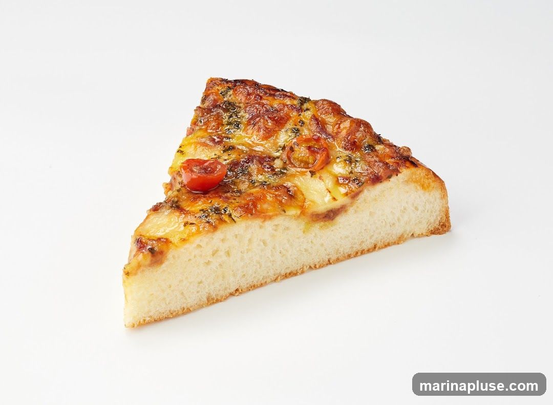 A single slice of pizza with a thick crust, topped with melted cheese, tomato sauce, and cherry tomatoes. The pizza is presented against a plain white background.