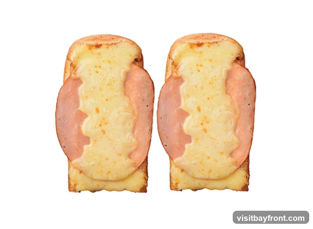 Two pieces of toast topped with melted cheese and a slice of ham. The toast is golden brown, and the cheese is bubbly and slightly browned in spots. The ham is pink and oval-shaped, covering the center of the toast.