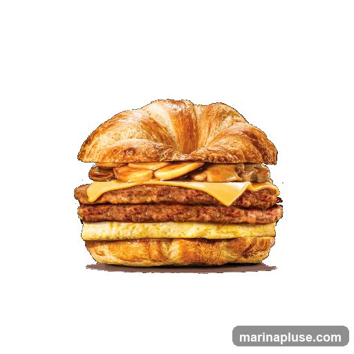 A close-up studio shot of a breakfast sandwich on a black background. The sandwich is made with a croissant bun, layered with two sausage patties, a slice of melted cheese, scrambled eggs, and topped with what appears to be sautéed mushrooms and onions.