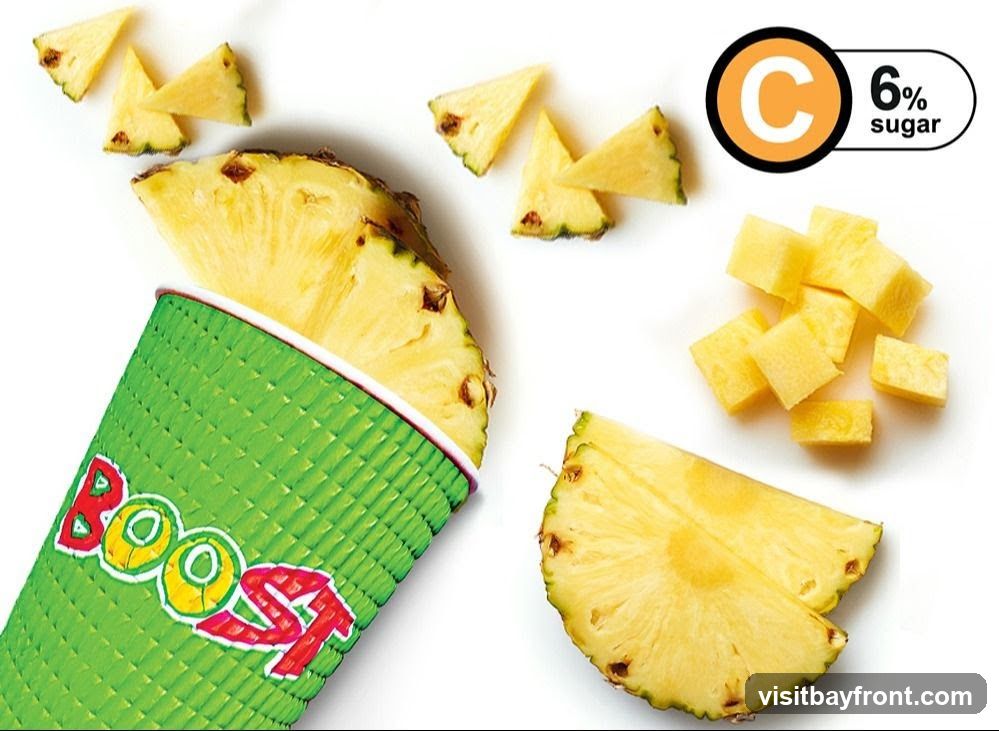 A green textured cup with the word "Boost" in colorful letters is shown. Slices and cubes of fresh pineapple are scattered around the cup. A graphic indicates "C" and "6% sugar".