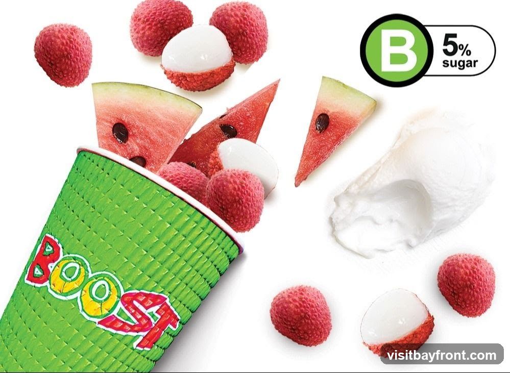 A green cup with the word "Boost" in colorful letters is tilted, spilling out lychees and slices of watermelon. Several whole lychees, peeled lychees, and watermelon slices are scattered around the cup. A dollop of white cream or yogurt is also visible. A circular logo with a green "B" and the text "5% sugar" is in the upper right corner.