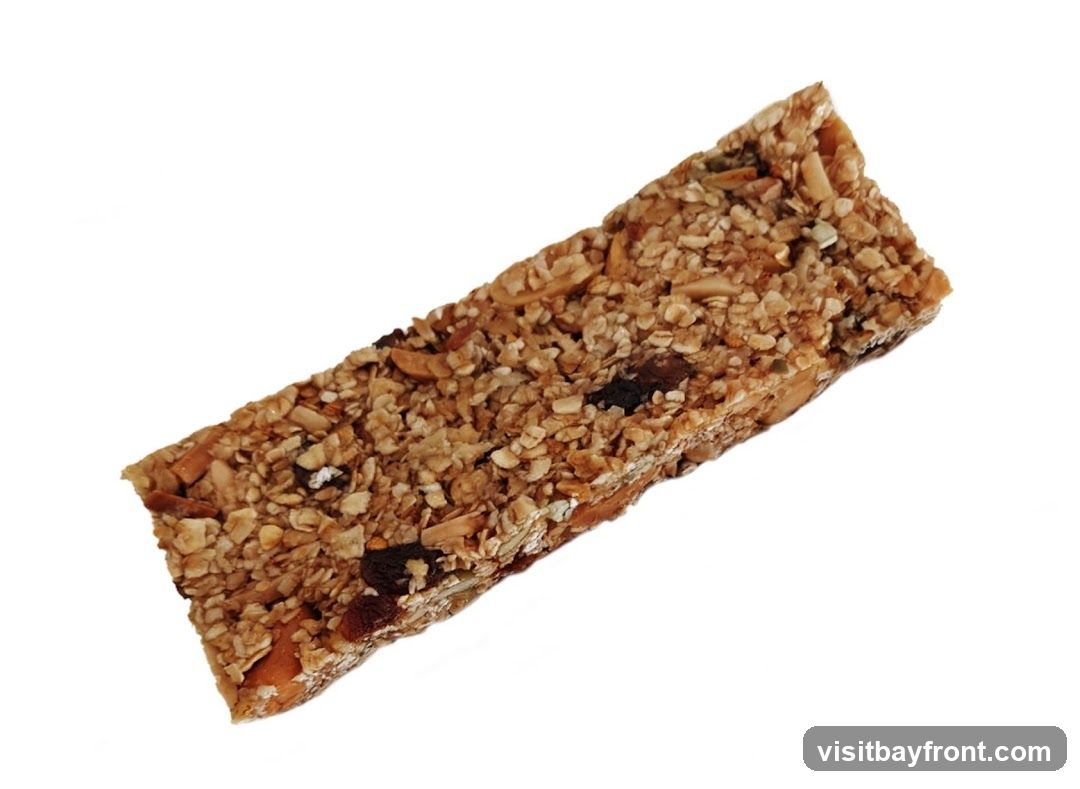 A close-up, isolated shot of a granola bar on a white background. The bar is rectangular and appears to be made of oats, nuts, seeds, and dried fruit, bound together.