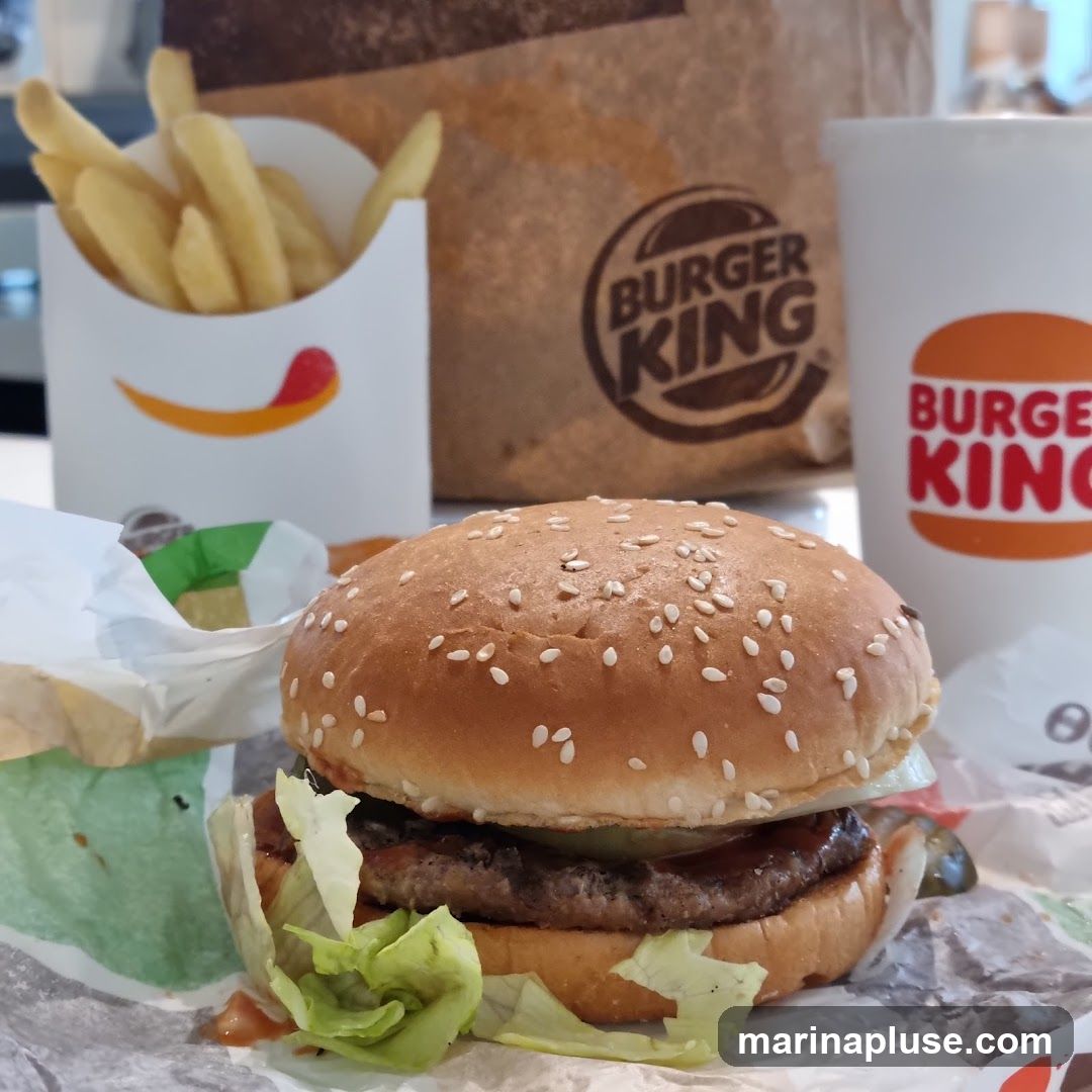 A close-up shot of a Burger King meal, featuring a Whopper burger, french fries, and a drink. The Burger King logo is visible on the paper bag and the cup.