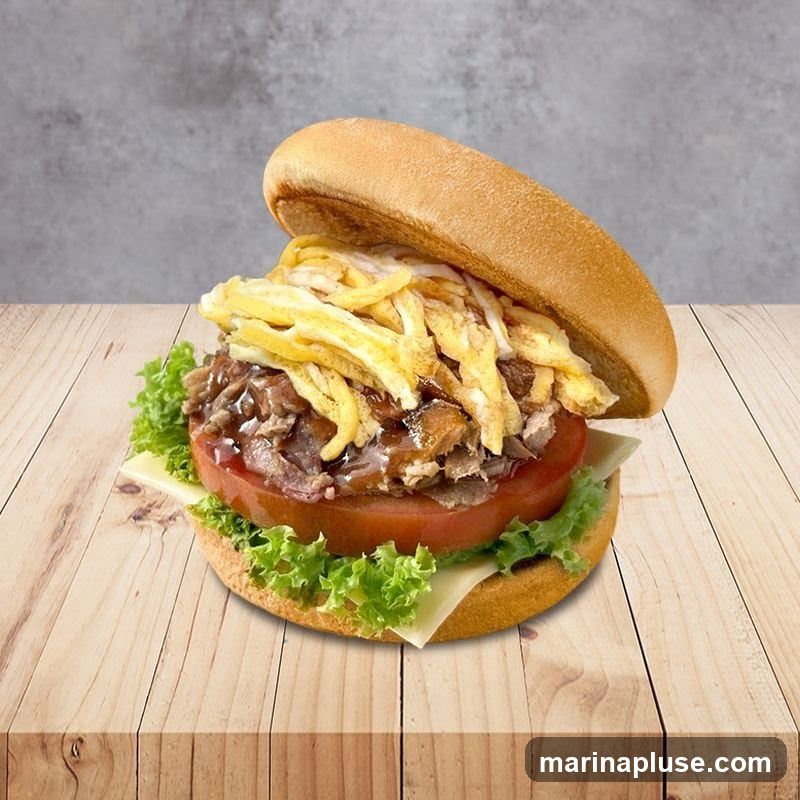 A close-up shot of a burger on a wooden table. The burger is made with a soft bun, lettuce, tomato, cheese, shredded meat with sauce, and thin strips of egg. The background is a textured gray wall.