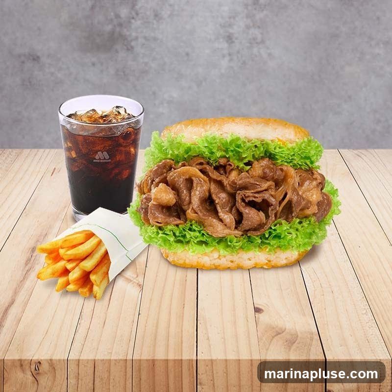 A beef burger with lettuce, a glass of cola with ice, and a serving of french fries on a wooden table. The cola glass has a logo on it.