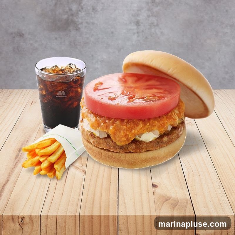 A burger with a large slice of tomato, french fries, and a cola drink with ice. The burger has two patties, sauce, and onions. The fries are in a white paper wrapper. The cola has a logo on the glass.