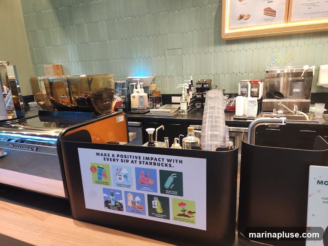 A view of a Starbucks counter with coffee beans in a grinder, various dispensers, cups, and a sign promoting positive impact. The background features light green tiled walls.