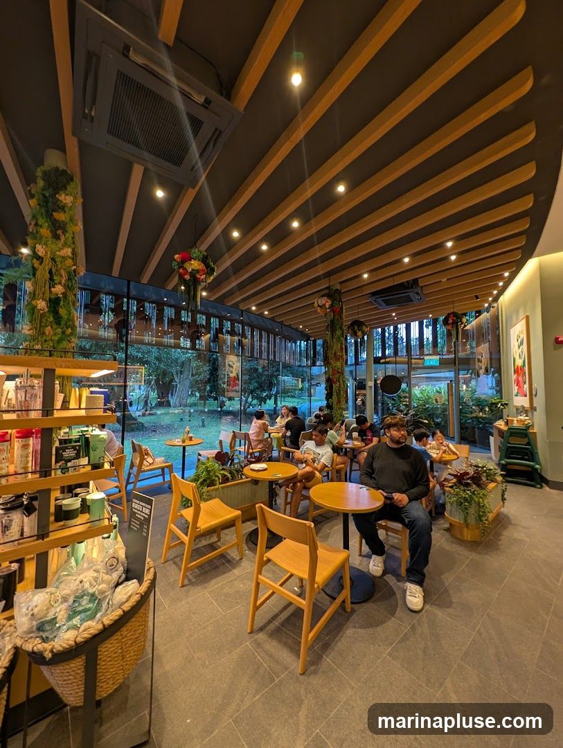 The image shows the interior of a cafe with several customers seated at tables. The cafe has a modern design with wooden beams on the ceiling and large windows overlooking an outdoor area. There are shelves stocked with merchandise, and plants are used as decoration.