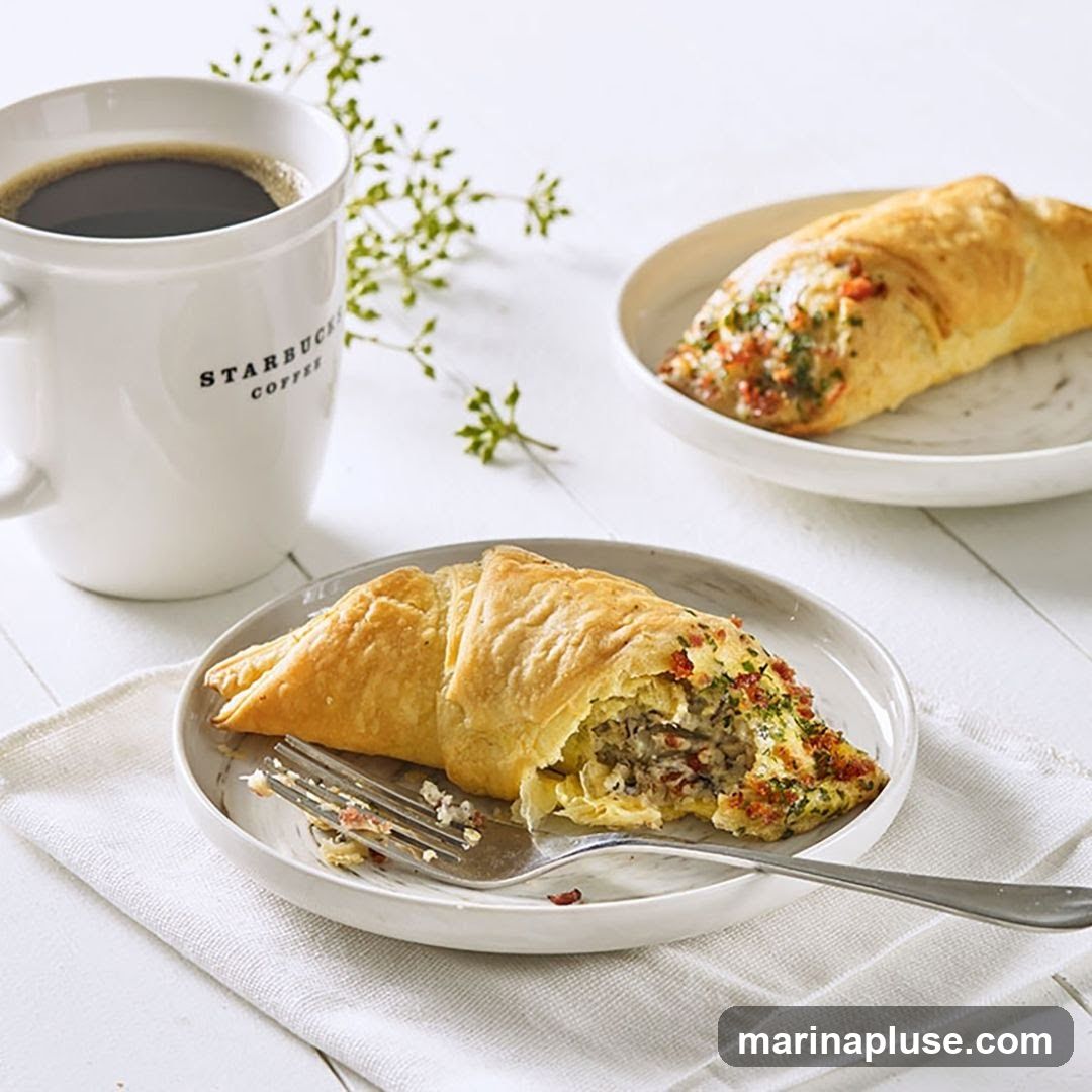 A white mug with the Starbucks Coffee logo sits next to two pastries on plates. One pastry is partially eaten, with a fork resting on the plate. The other pastry is whole and sits on a separate plate. A sprig of greenery is placed between the mug and the pastries. The background is a white wooden surface.