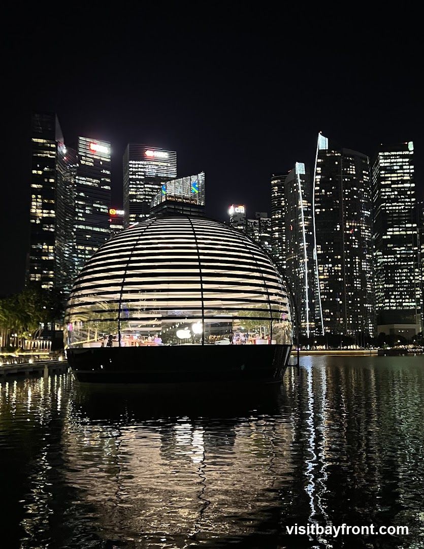 A nighttime view of the Singapore skyline featuring the illuminated Marina Bay Sands hotel towers in the background and the distinctive dome-shaped Esplanade – Theatres on the Bay in the foreground, reflecting on calm water.
