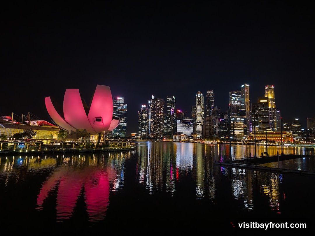 Night view of Singapore's skyline with illuminated skyscrapers and the ArtScience Museum reflecting on water.