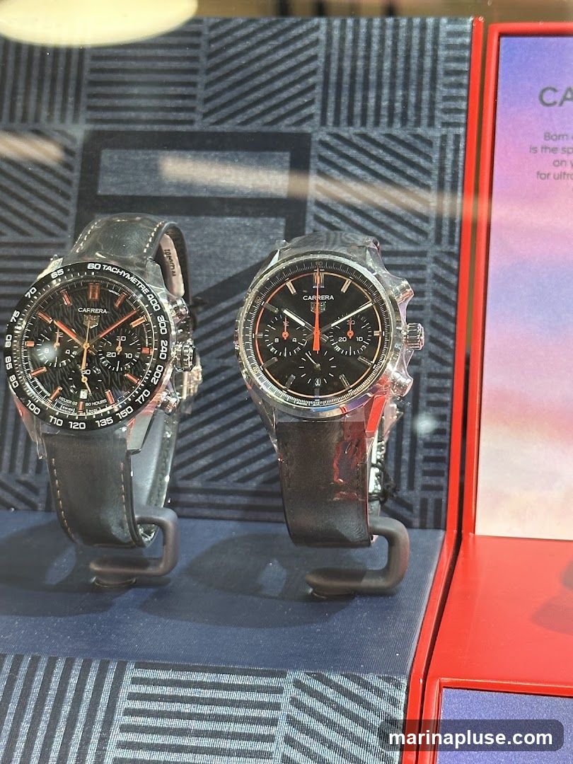 Two black leather strap watches with black faces and orange accents are displayed on stands. The watch on the left has a tachymeter bezel. A red display box with text is to the right.
