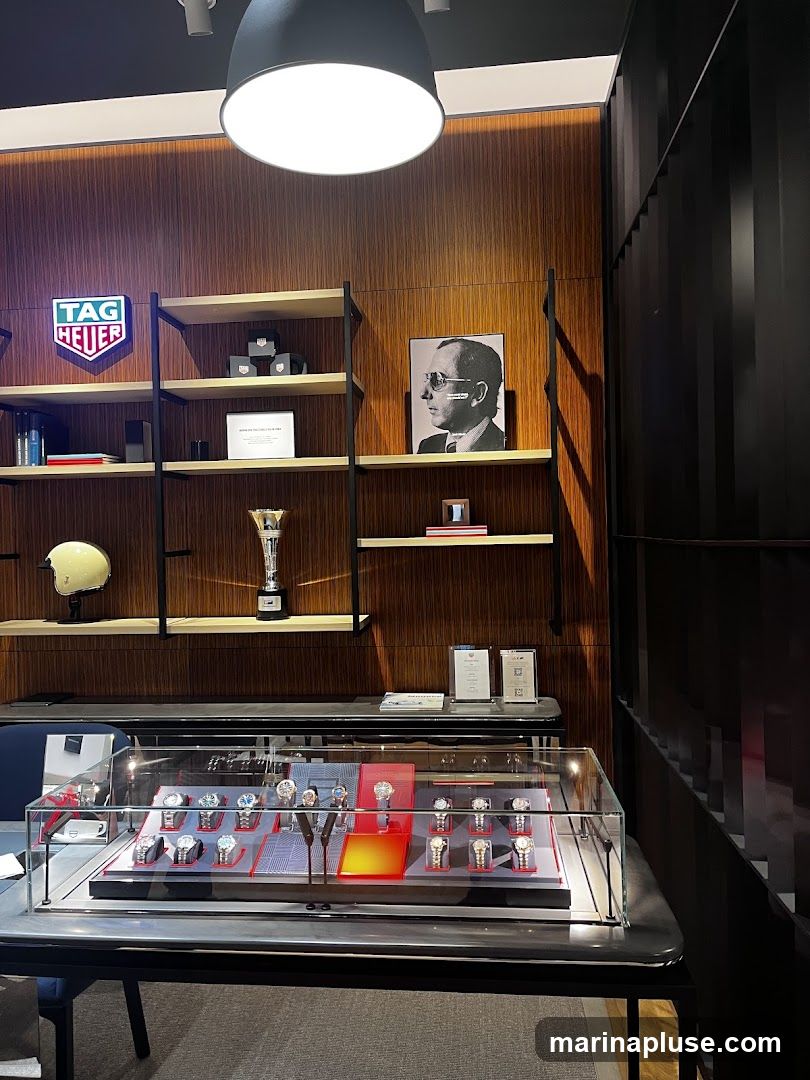 A display case filled with TAG Heuer watches is showcased in a store. Above the display, shelves hold various items including a trophy, a helmet, and framed pictures. A neon TAG Heuer sign is visible on the wall.