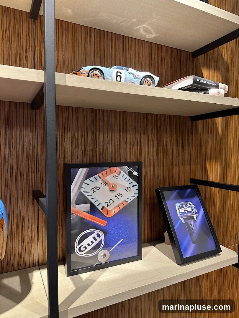 Two shelves are visible, with a wood-paneled background. The top shelf holds a model of a blue and orange Gulf racing car with the number 6, and two books. The bottom shelf displays a framed picture of a Gulf logo and a clock face, and another framed picture of a blue watch.