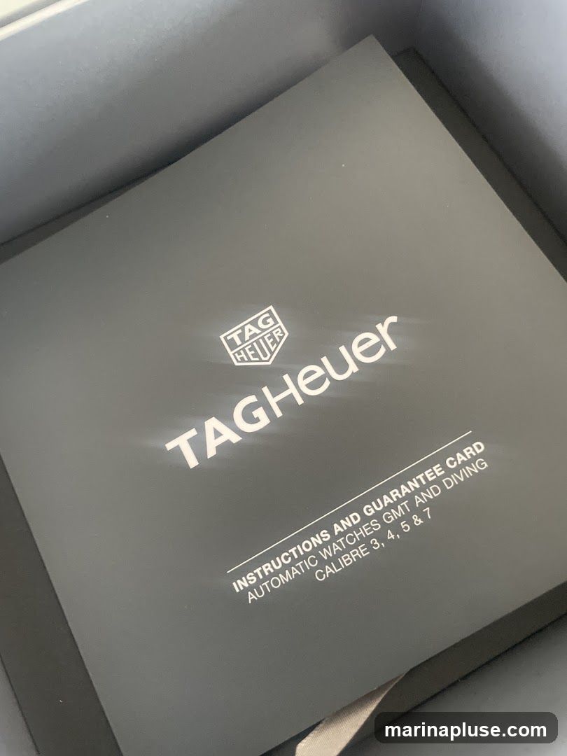 A close-up shot of a dark gray booklet with the TAG Heuer logo and name prominently displayed in white. Below the logo, text reads "INSTRUCTIONS AND GUARANTEE CARD AUTOMATIC WATCHES GMT AND DIVING CALIBRE 3, 4, 5 & 7". The booklet appears to be inside a box.