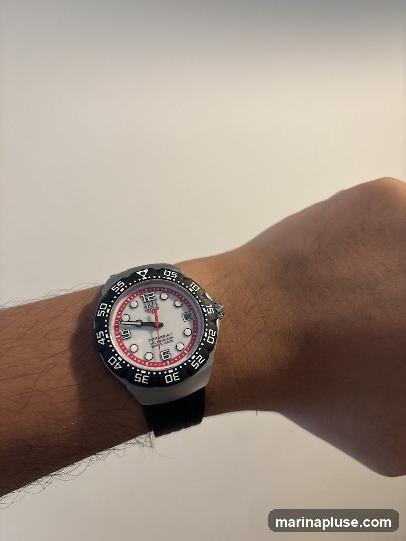 A close-up shot of a TAG Heuer Formula 1 watch on a person's wrist. The watch has a white dial with red accents and a black strap. The bezel is black and white with minute markers. The watch face displays the TAG Heuer logo,