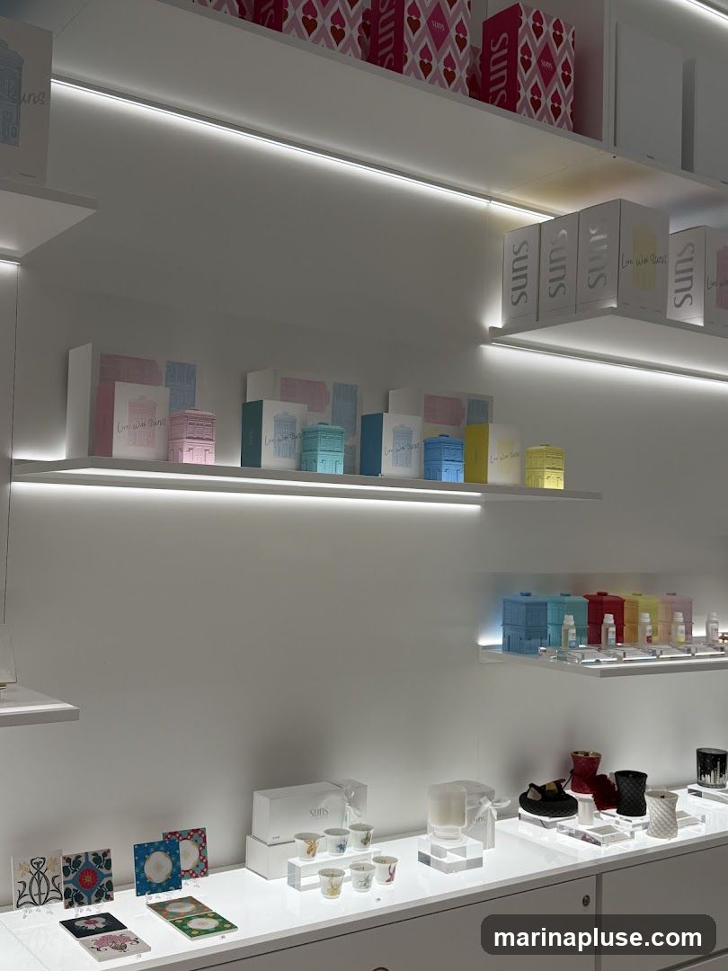 Shelves are stocked with various items, including decorative boxes, small cups, and candles. The items are arranged neatly on white shelves with integrated lighting. Some boxes have the brand name 'Suns' visible.