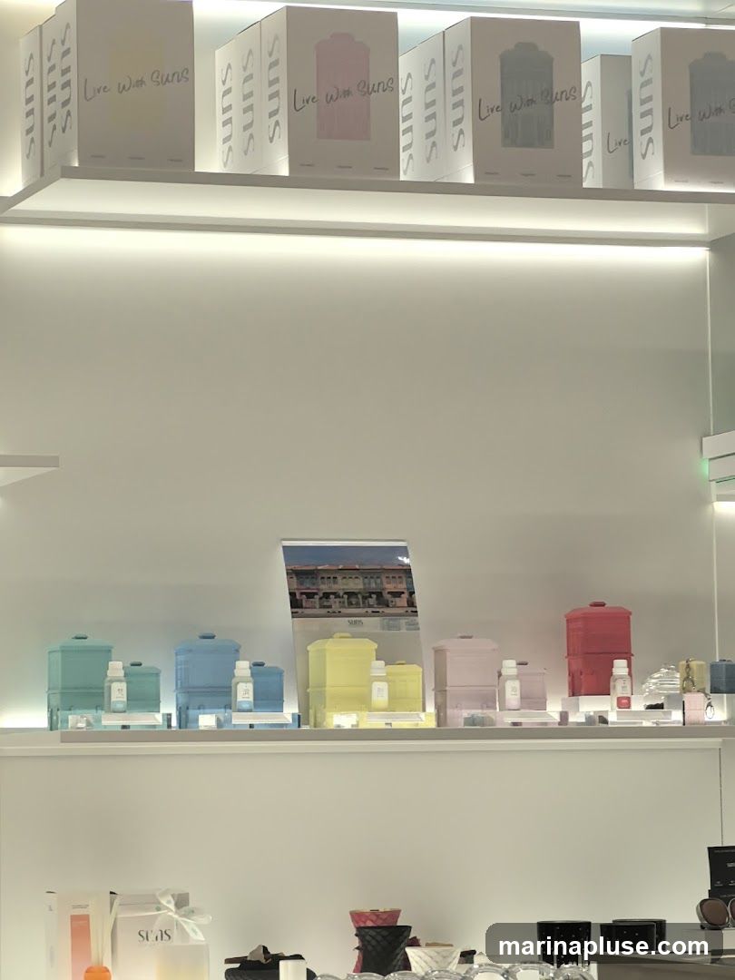 A retail display featuring various products on shelves. The top shelf shows boxes with the branding "Live With Suns" and "suns". The middle shelf displays colorful containers and bottles, with a promotional image of colorful buildings in the background. The bottom shelf shows more packaged items and decorative objects.