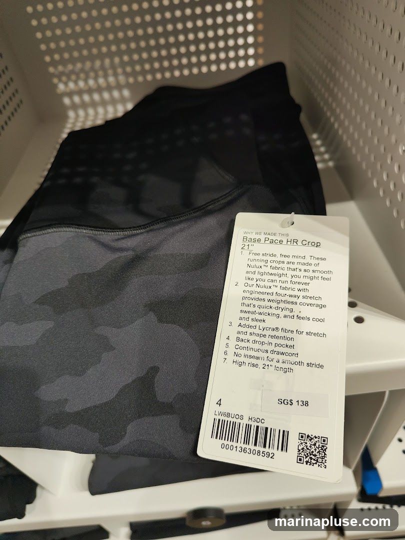 A pair of black and grey camouflage Lululemon Base Pace HR Crop pants with a tag. The tag details the features of the pants, including the fabric, fit, and price.