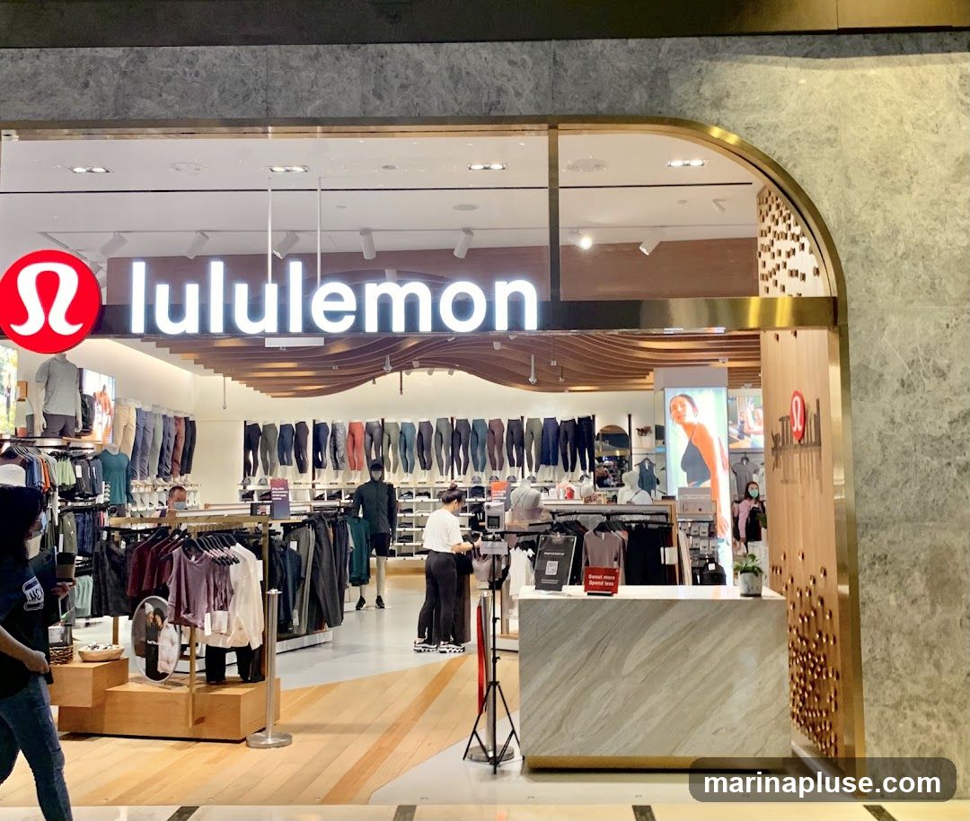 The exterior of a Lululemon store with the brand's logo and name prominently displayed above the entrance. Inside, athletic apparel is displayed on racks and mannequins. Customers and staff are visible within the store.