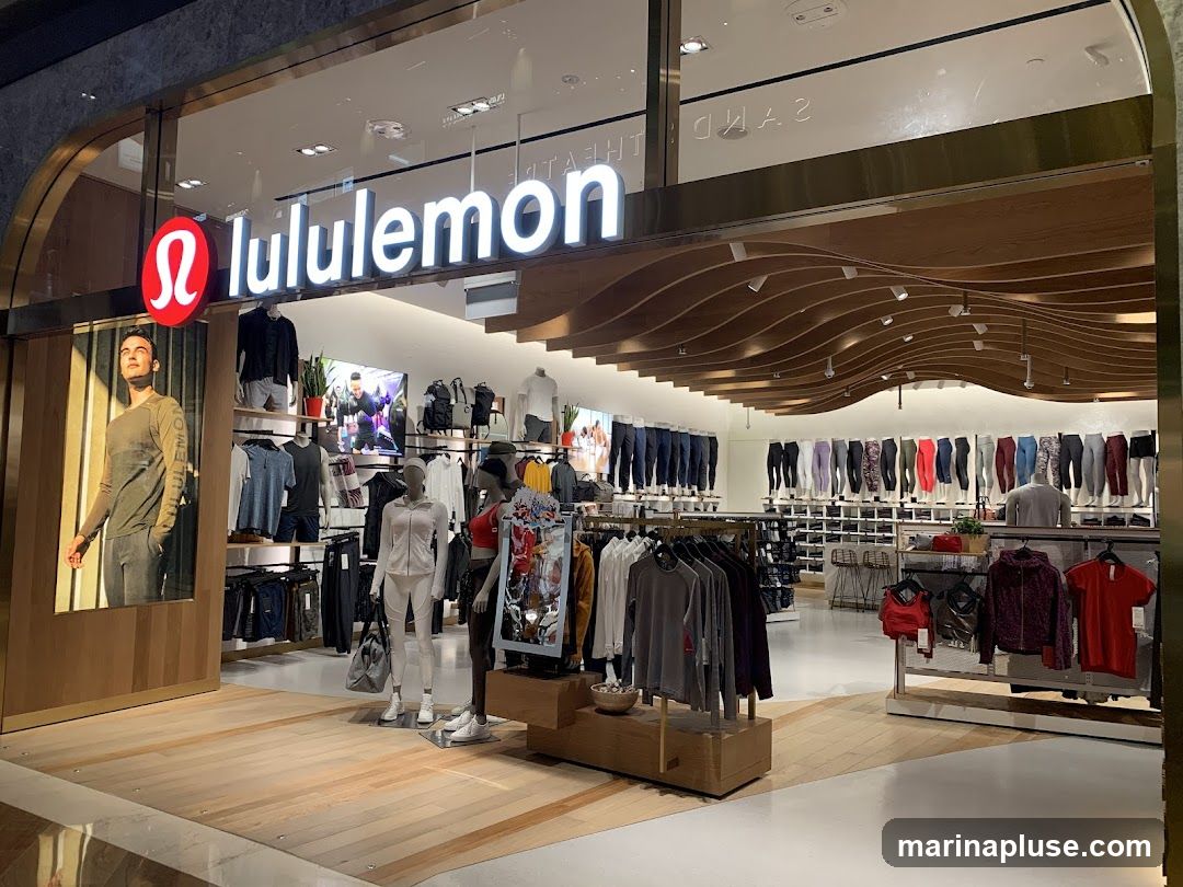 The exterior of a Lululemon store with its prominent logo and name displayed above the entrance. Inside, mannequins are dressed in athletic wear, and racks of clothing are visible, showcasing a variety of activewear. The store features a modern design with wooden accents on the ceiling and floor.