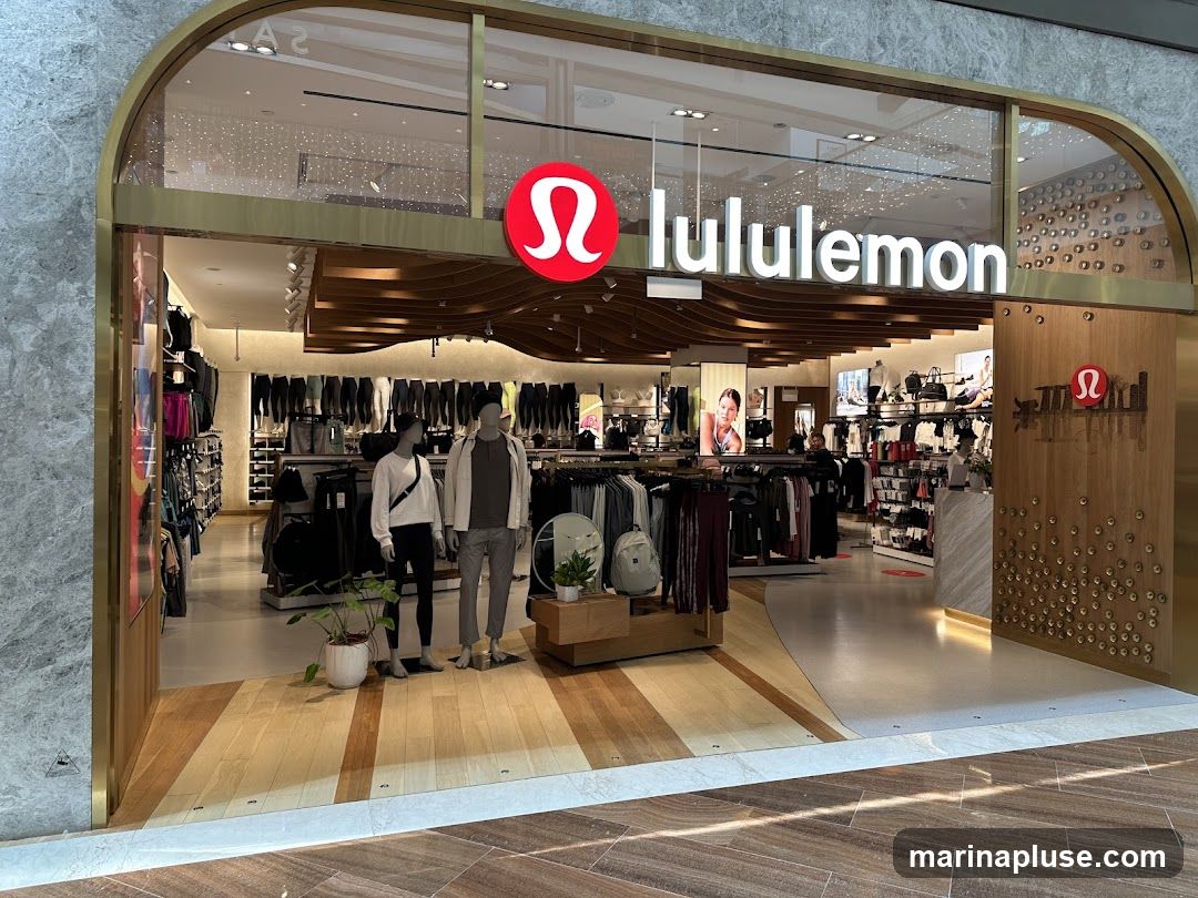The exterior of a Lululemon store. The store has a large glass entrance with the Lululemon logo and name displayed prominently above the entrance. Inside, clothing racks and mannequins display athletic wear. The store interior features wooden accents and modern lighting.