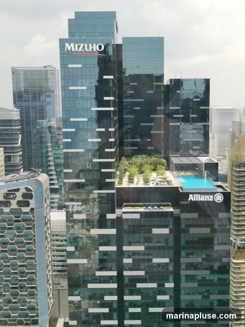 A view of modern skyscrapers, including the Mizuho building with its prominent logo and the Allianz building with a swimming pool on its rooftop. The buildings are characterized by their glass facades and contemporary architectural design.