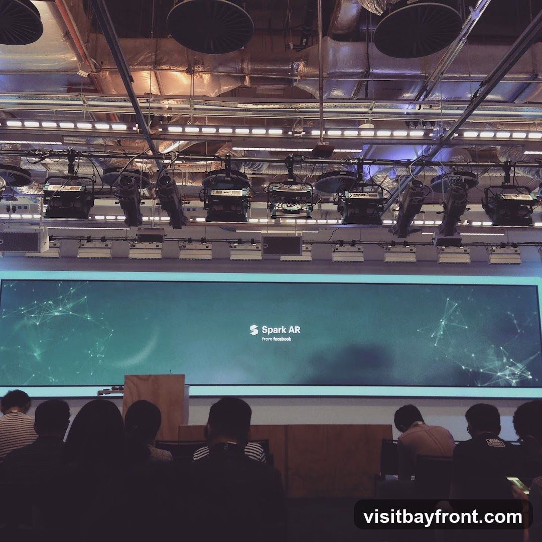 An audience watches a presentation on a large screen displaying "Spark AR from Facebook." The screen is set against a backdrop of stage lighting and equipment.