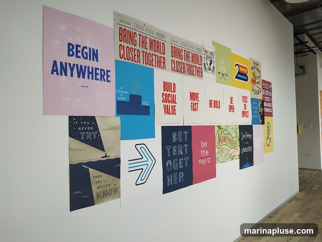 A collection of motivational posters and quotes are displayed on a white wall. The posters feature various phrases and designs, including "BEGIN ANYWHERE," "BRING THE WORLD CLOSER TOGETHER," "BUILD SOCIAL VALUE," "MOVE FAST," "BE BOLD," "BE OPEN," "FOCUS ON IMPACT," "IF YOU NEVER TRY, THEN YOU'LL NEVER KNOW," "BETTER TOGETHER," "be the hero," "KINDNESS," and "You Belong to the Universe." Some posters have illustrative elements like fireworks, a boat on the water, glasses, and a rainbow.