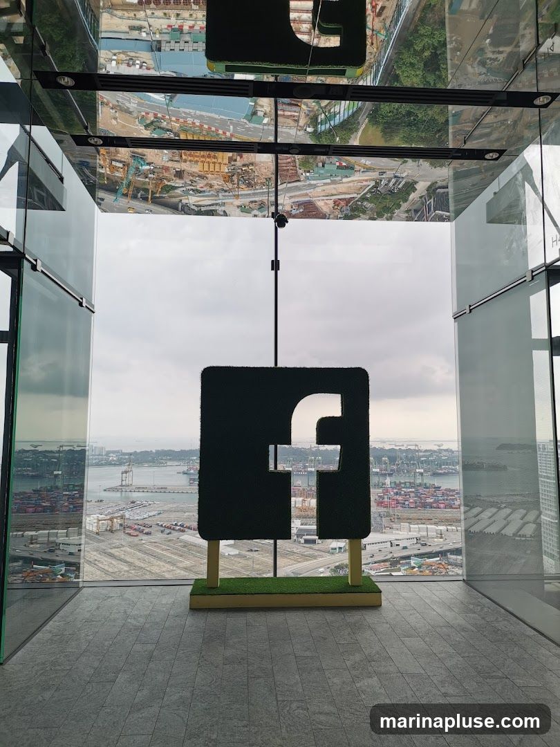 A large, dark green, grass-covered sign shaped like the Facebook 'f' logo is displayed indoors, with a panoramic view of a busy port and construction site visible through large windows. The ceiling is mirrored, reflecting the scene below and the cityscape.