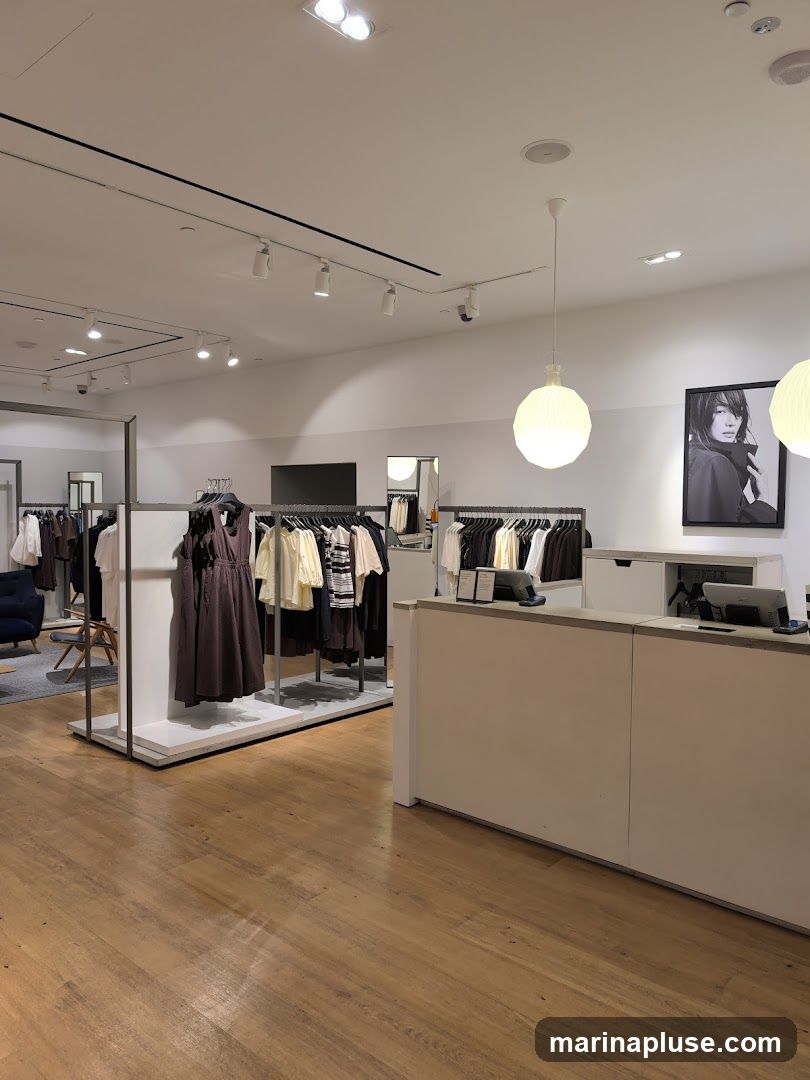 A well-lit clothing store interior with racks of women's apparel. A checkout counter is visible on the right, with a framed black and white photograph of a woman on the wall behind it. The floor is made of light-colored wood planks.