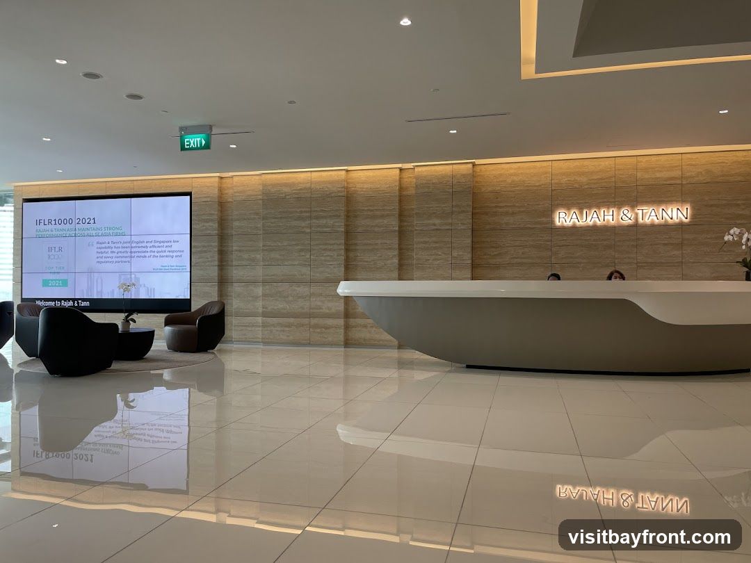 A modern office lobby with a large screen displaying company information, a reception desk with staff, and seating areas. The company name "RAJAH & TANN" is visible on the wall behind the reception desk.