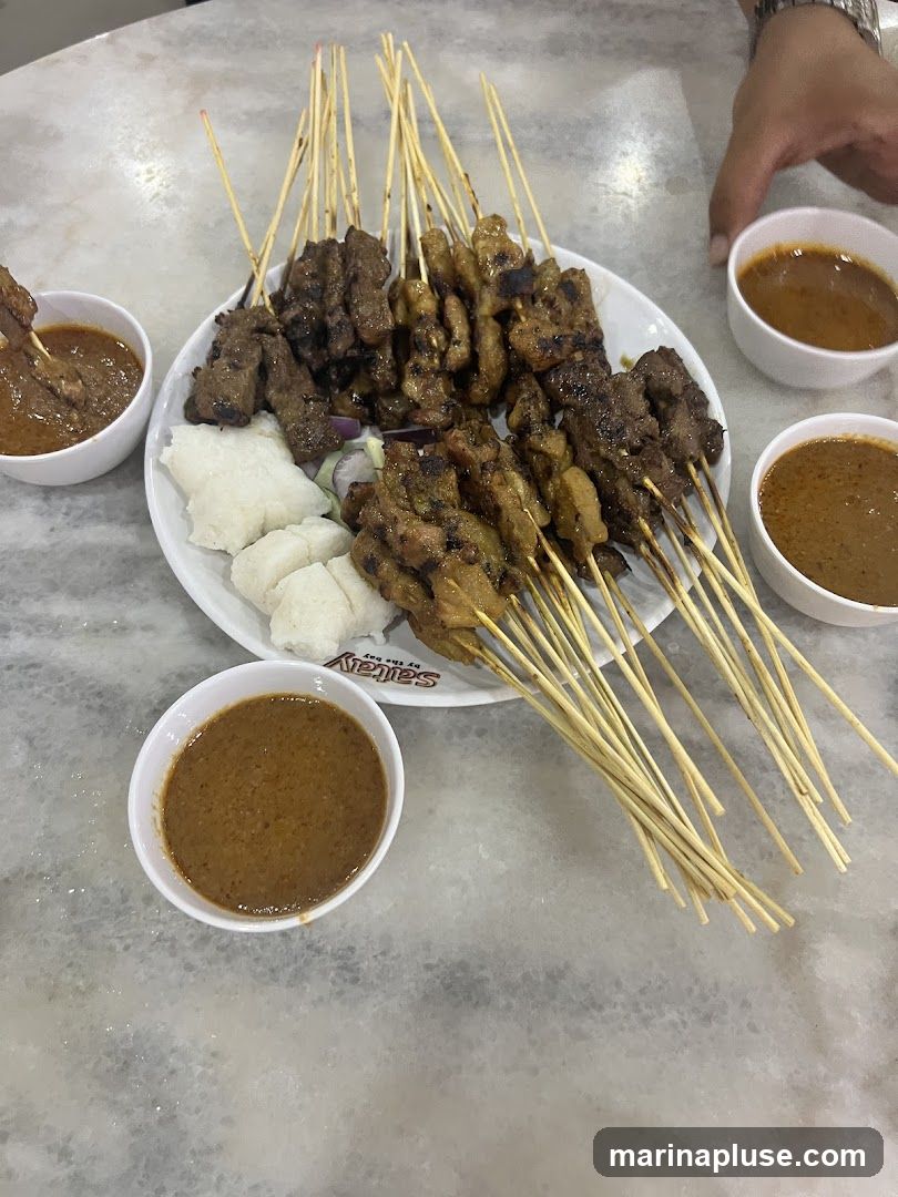 A plate of satay skewers with peanut sauce and rice cakes.