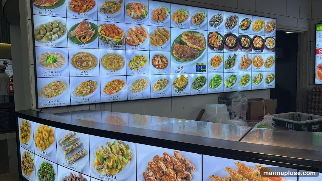 A brightly lit digital menu board displaying various seafood and noodle dishes with accompanying images.
