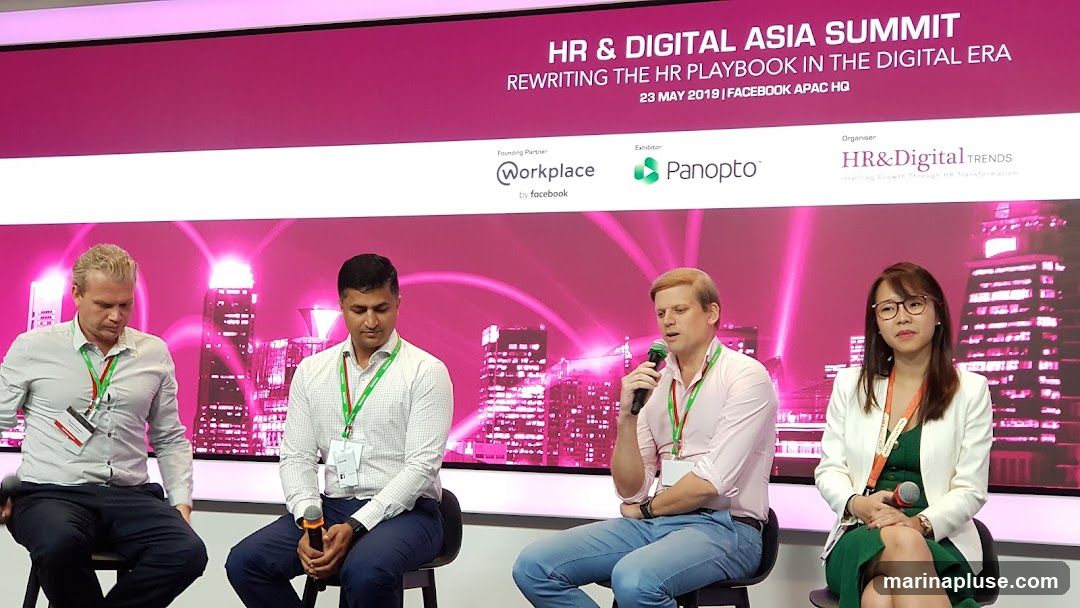 Four people are seated on a stage in front of a backdrop that reads "HR & DIGITAL ASIA SUMMIT REWRITING THE HR PLAYBOOK IN THE DIGITAL ERA 23 MAY 2019 | FACEBOOK APAC HQ". The backdrop also features logos for "Workplace by Facebook", "Panopto", and "HR&Digital TRENDS". The individuals appear to be panelists at a conference, with lanyards around their necks. One man is speaking into a microphone.