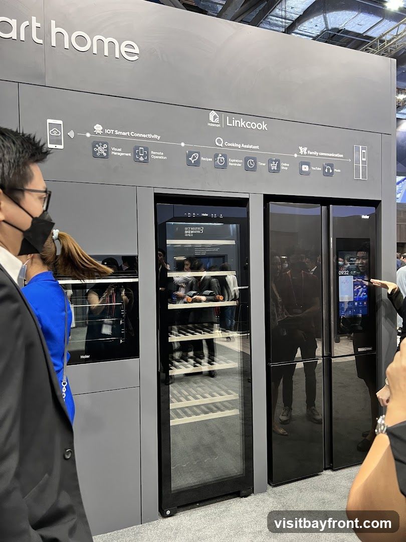 A display showcasing smart home appliances, including a wine cooler and a refrigerator with a touchscreen interface. The display highlights features like IOT Smart Connectivity and Cooking Assistant.