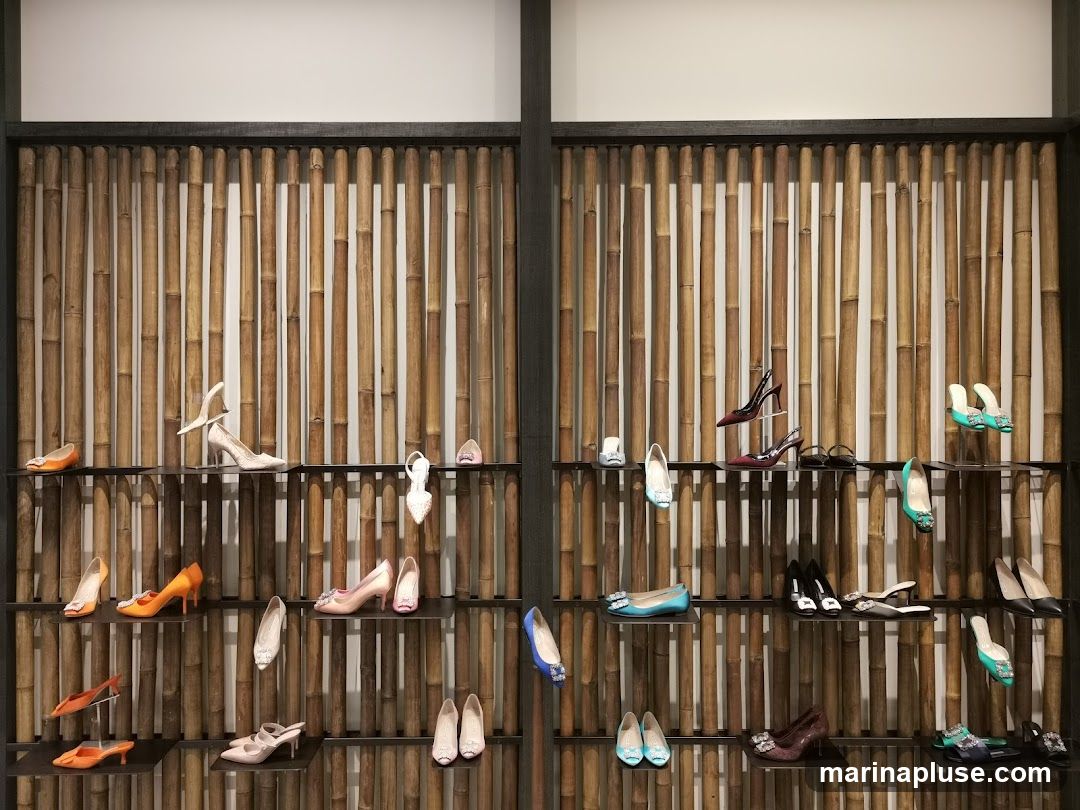 A wall display of various women's shoes on shelves against a bamboo backdrop. The shoes include heels, flats, and sandals in a range of colors and styles.