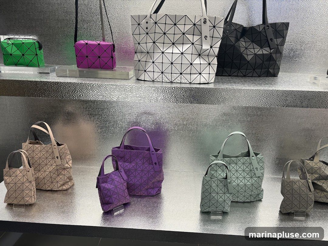 A display of various handbags and small purses with a distinctive geometric, triangular pattern. The bags are arranged on shelves with a textured, metallic silver background. Colors include green, purple, white, black, beige, and light grey.