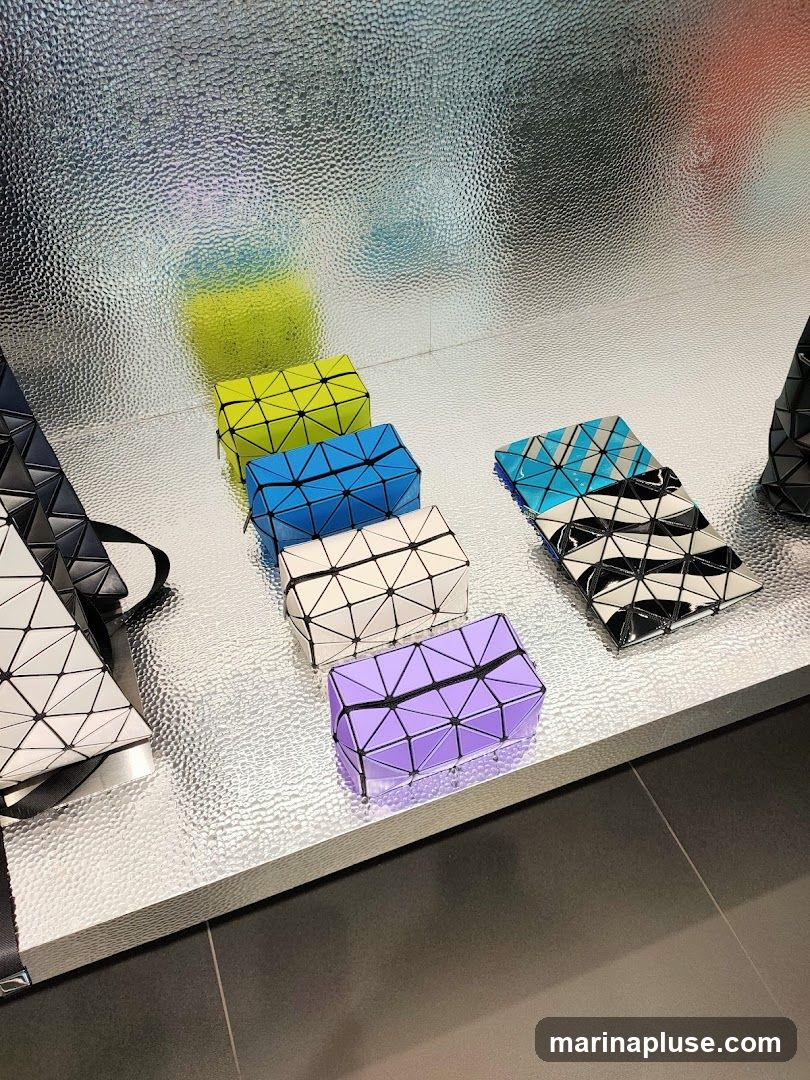 A display of geometric-patterned bags in various colors including lime green, blue, white, purple, and a black and white patterned clutch. The bags are arranged on a textured silver surface with a reflective, textured background.