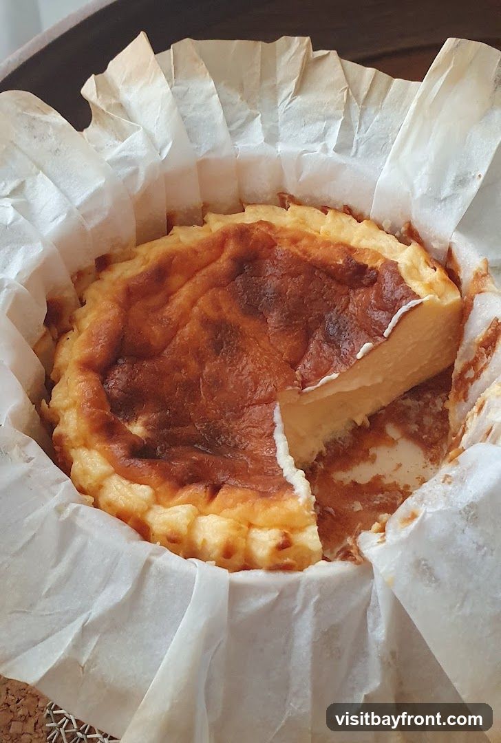 A close-up shot of a burnt Basque cheesecake, with a slice removed. The cheesecake has a dark, caramelized top and a creamy, pale yellow interior. It is presented in a white parchment paper liner within a basket.