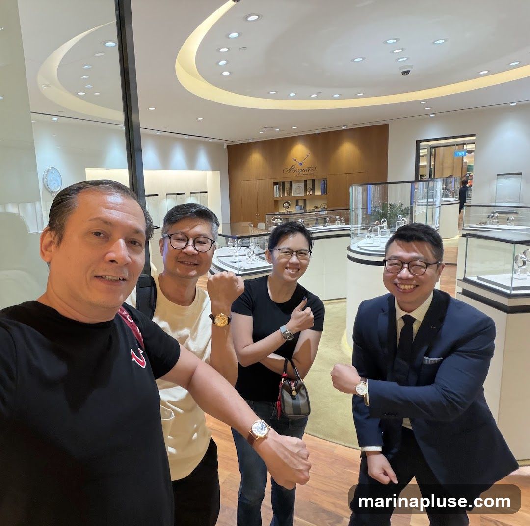 Four people are posing for a selfie in a well-lit store that appears to be a watch retailer. The individuals are smiling and showing off watches on their wrists. In the background, display cases filled with watches are visible, along with branding that reads "Breguet". The store has a modern and luxurious interior design.