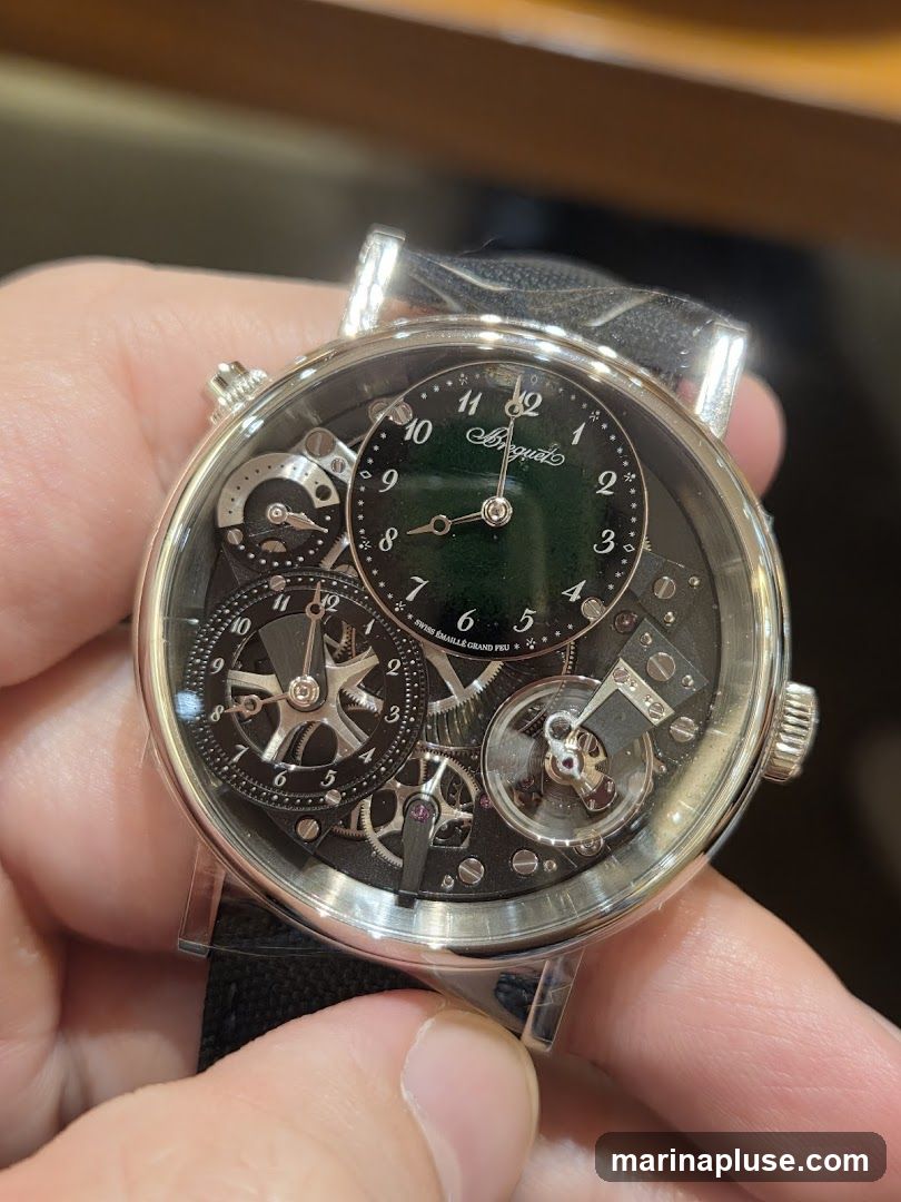 A close-up shot of a Breguet watch with a black dial and intricate mechanical details. The watch features a smaller sub-dial for timekeeping with Roman numerals and a larger exposed movement with gears and springs. The brand name "Breguet" is visible on the sub-dial.
